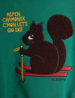 Close-up of a green sweatshirt featuring a brown chenille skiing squirrel patch with skis and yellow text.