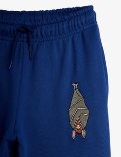 Close-up of blue sweatpants featuring an elastic waistband with a drawstring and a bat embroidery on the leg.