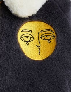 Close-up of a dark grey faux fur aviator jacket featuring a round yellow embroidered face patch.