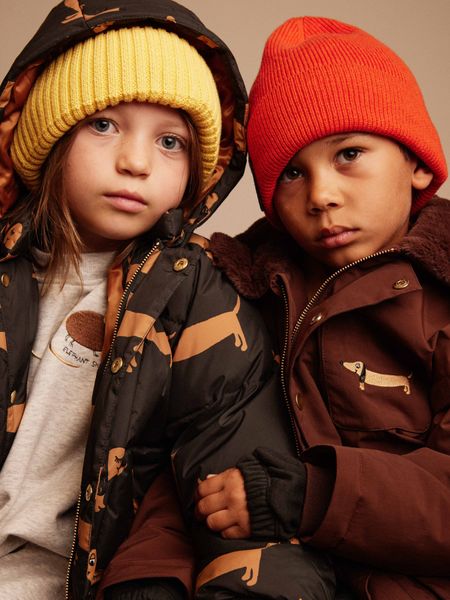 Two children wearing colorful ribbed hats and winter jackets.