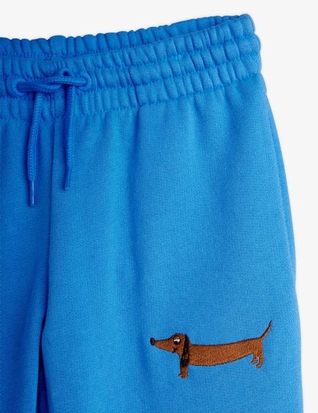 Close-up of the front of blue sweatpants featuring an adjustable drawstring waist and a brown dog embroidery.