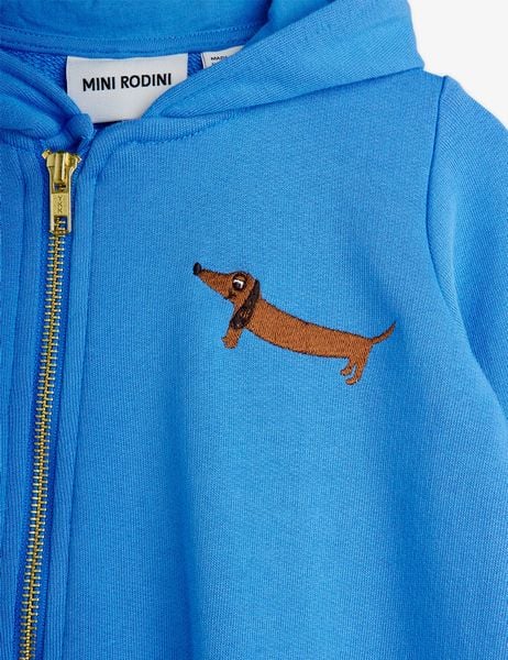 Close-up of a blue baby onesie featuring an embroidered brown dog on the chest and an asymmetrical zipper.