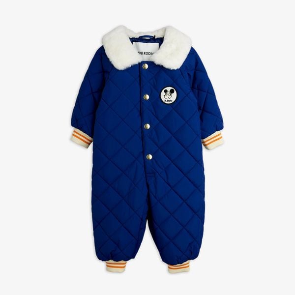 Blue quilted baby overall with a white faux-fur collar, Ritzratz patch, and striped ribbed cuffs.