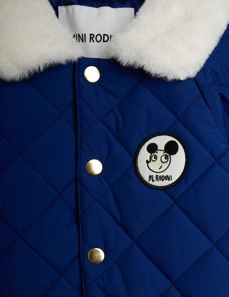 Close-up of the blue quilted baby overall showing gold snap buttons, a white faux-fur collar, and a Ritzratz patch.