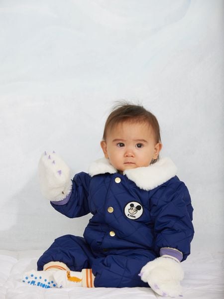 Blue quilted baby overall with a white faux-fur collar, snap buttons, and a Ritzratz chest patch.