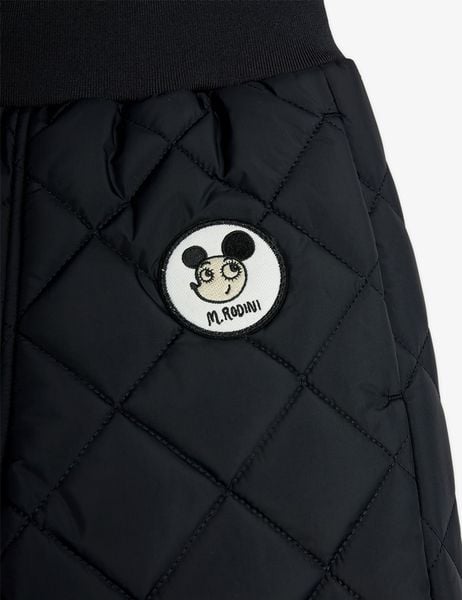 Close-up of a black quilted outerwear trousers featuring a round Ritzratz character patch.