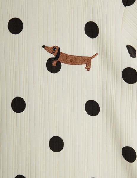Close-up of off-white ribbed fabric featuring a black dot pattern and an embroidered brown dachshund.