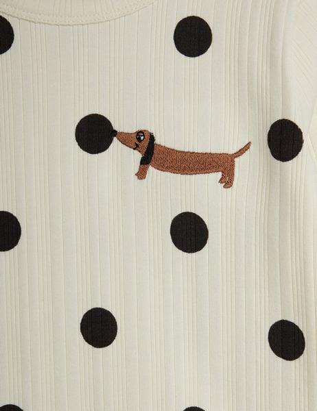 Close-up of off-white ribbed fabric with black polka dots and an embroidered brown dog motif.