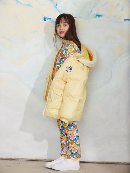 Yellow heavy puffer jacket with a Ritzratz patch and hood, worn over a floral outfit.
