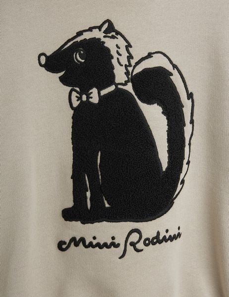 Close-up of the black skunk chenille artwork with a bow tie and script logo on grey fabric.