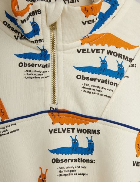 Close-up of cream sweatshirt featuring a gold half-zip and blue and orange Velvet worms print.