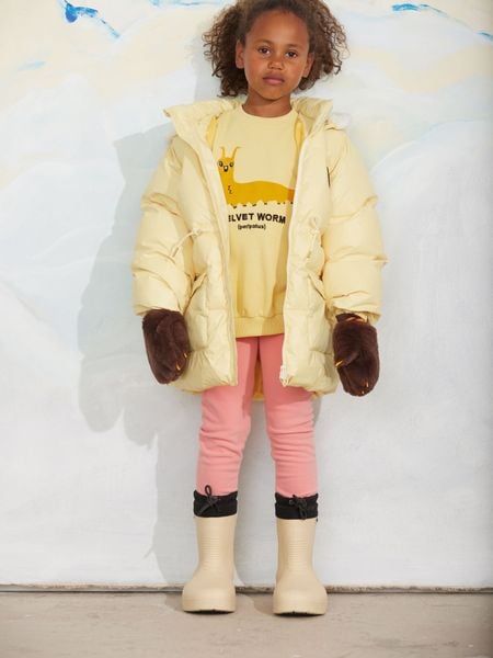 Yellow organic cotton sweatshirt featuring a Velvet worm print, worn with a yellow puffer jacket and brown mittens.