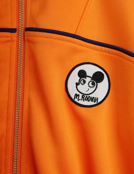 Orange recycled polyester tracksuit jacket detail featuring a circular Ritzratz patch and gold zipper.
