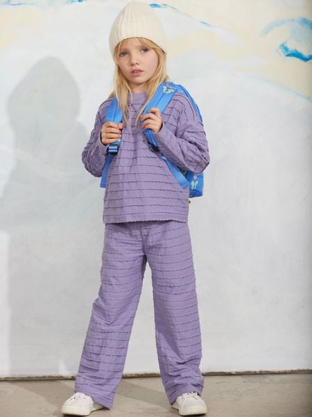 Purple textured long-sleeved top and matching trousers with frills, worn with a blue backpack.