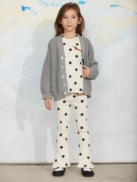 Grey melange knitted cardigan worn over an offwhite patterned top and trousers, featuring a V-neck and white buttons.