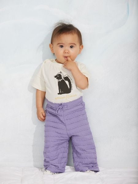 Purple textured frill trousers and an off-white top featuring a skunk print, worn by a child.