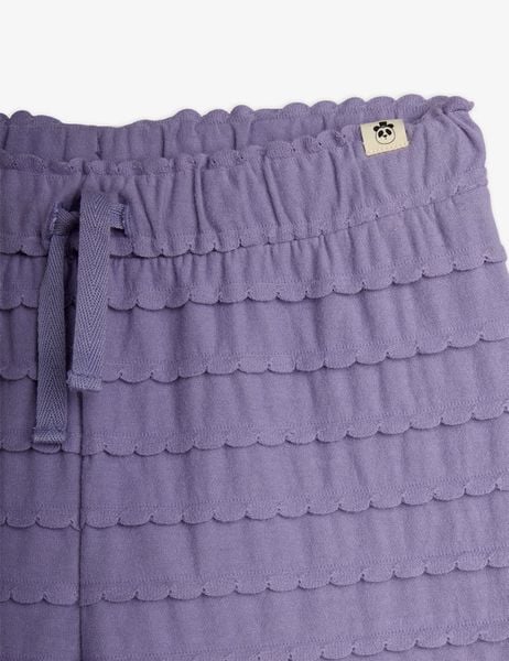 Close-up of purple trousers featuring horizontal frills with scalloped edges, drawstring waist, and a panda label.