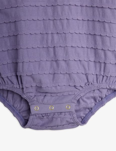 Close-up of a purple bodysuit featuring textured horizontal scalloped frills and snap buttons at the crotch.