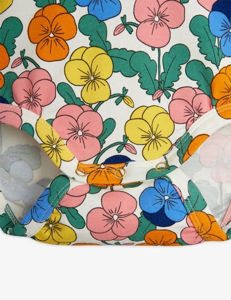 Close-up of a white bodysuit with a colorful Viola flower print and gold-tone snap buttons.