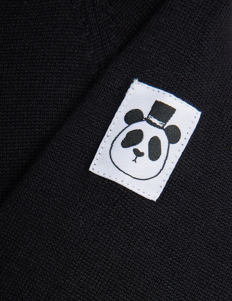Close-up of a white brand label featuring a panda with a top hat on a black knit jumpsuit.