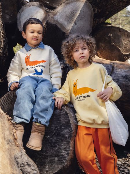 Orange Ritzratz patch trousers in recycled polyester with side piping, worn by a child in a yellow sweatshirt.