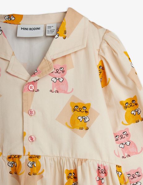 Close-up of a cream-colored dress featuring a Kittens print, pointed collar, and pink buttons.