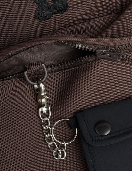 Close-up of a brown backpack showing a zipper and a black mini bag with a chain clip.