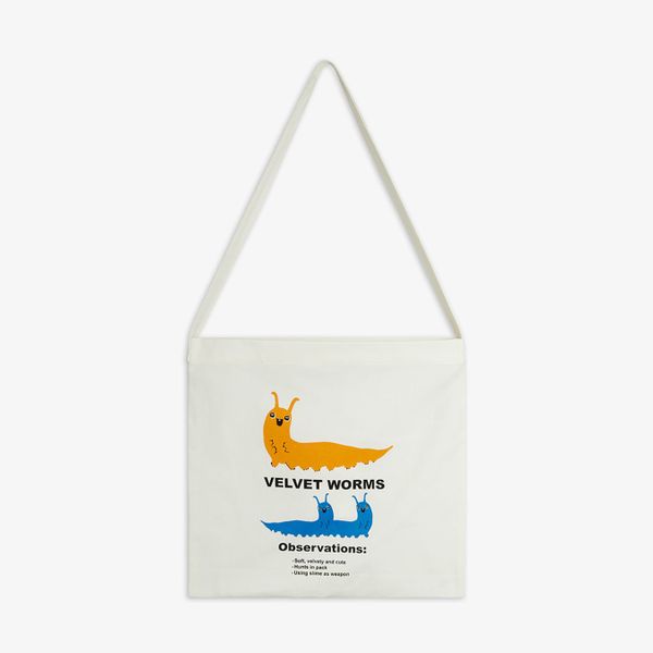 Off-white tote bag featuring a yellow and blue Velvet worm print and long top handles.
