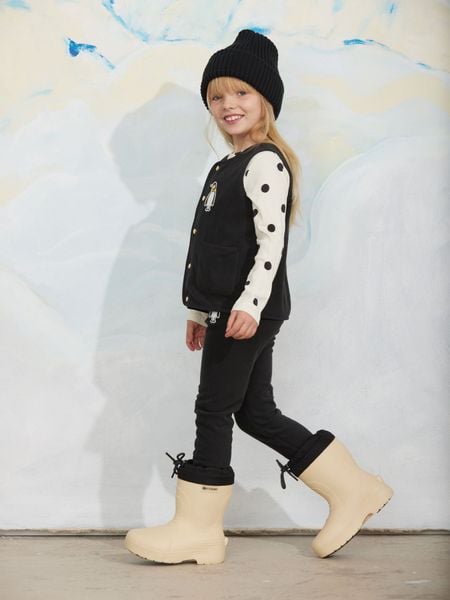 Black microfleece vest with penguin patch and front pockets, worn by a child walking in boots.