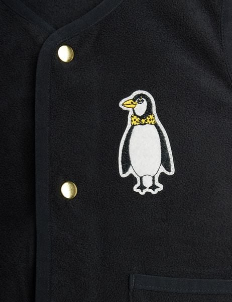 Close-up of a penguin patch and gold snap buttons on a black fleece vest.