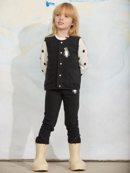 Black microfleece vest featuring a penguin patch and front pockets, worn by a child.
