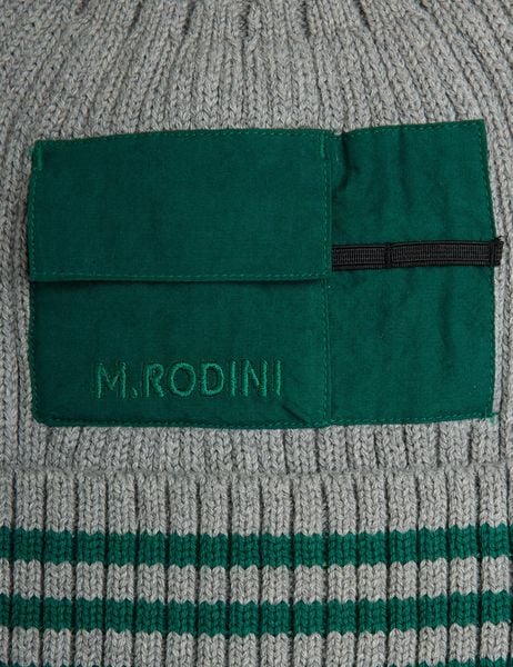 Close-up of a green woven pocket with logo embroidery on a grey ribbed hat with green stripes.