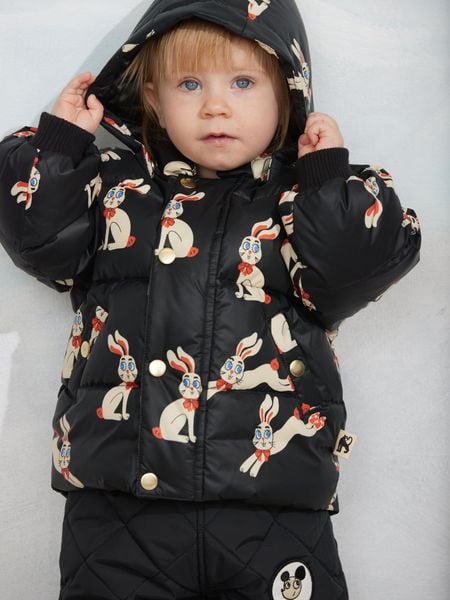 Black hooded puffer featuring a rabbit print and gold-colored snap buttons, worn by a child.