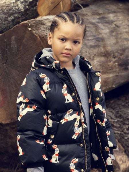 Black hooded puffer jacket featuring a Rabbit print, worn by a child outdoors.