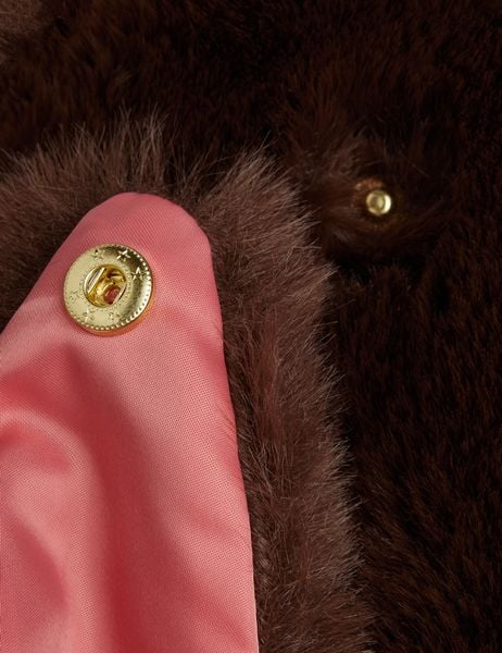 Brown faux fur jacket close-up showing a gold star-engraved snap button and coral lining.