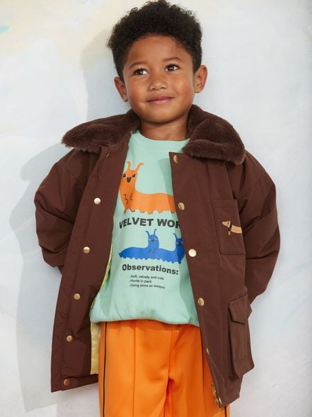 Brown padded nylon parka with faux fur collar and dachshund embroidery, worn by a child.