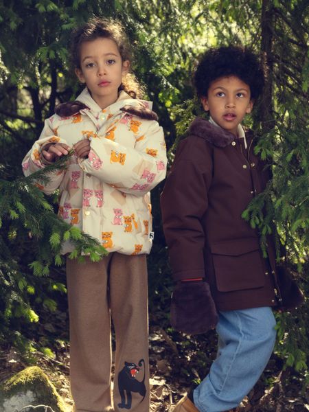 Brown padded parka with faux fur collar worn by a child standing outdoors among trees.