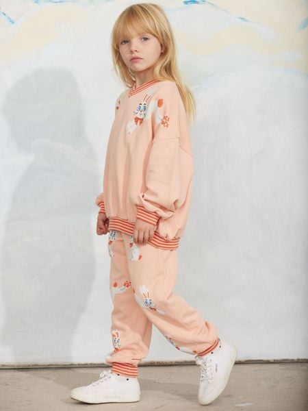 Pink sweatshirt and matching trousers with a Rabbits print and striped ribbed trims, worn by a child.