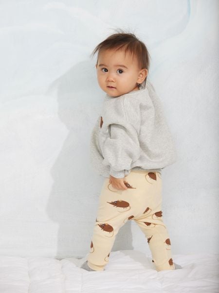 Grey melange sweatshirt and light yellow trousers with an elephant shrew pattern, worn by a child.