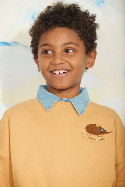 Close-up of a child wearing a beige sweatshirt with an embroidered Elephant shrew and a light blue collar.