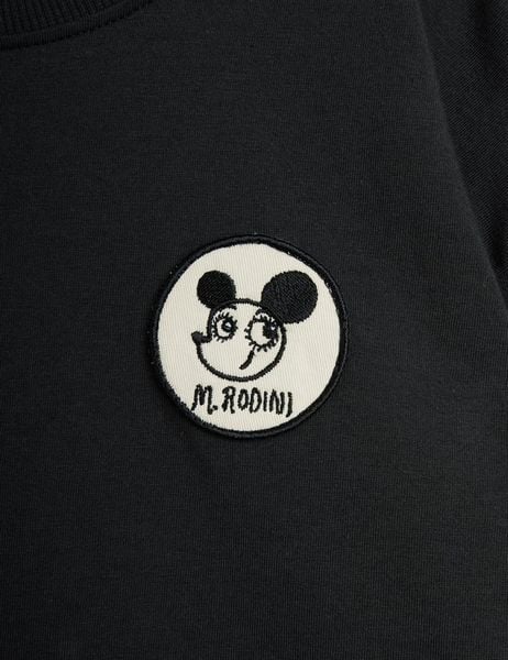 Circular white patch featuring a Ritzratz motif and black text on a black long-sleeved top.
