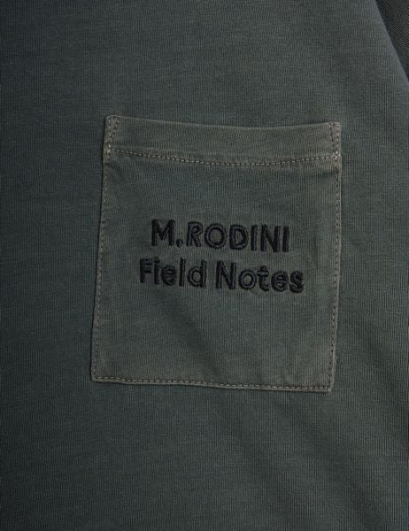 Close-up of a grey chest pocket featuring dark M.RODINI Field Notes embroidery.