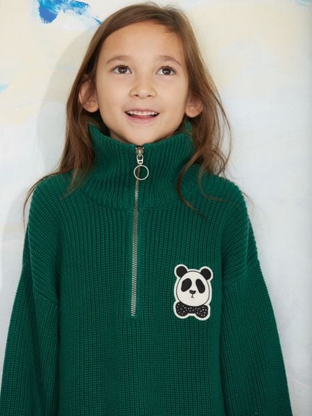 Close-up of a green chunky knit half-zip sweater with a panda patch on the chest, worn by a child.
