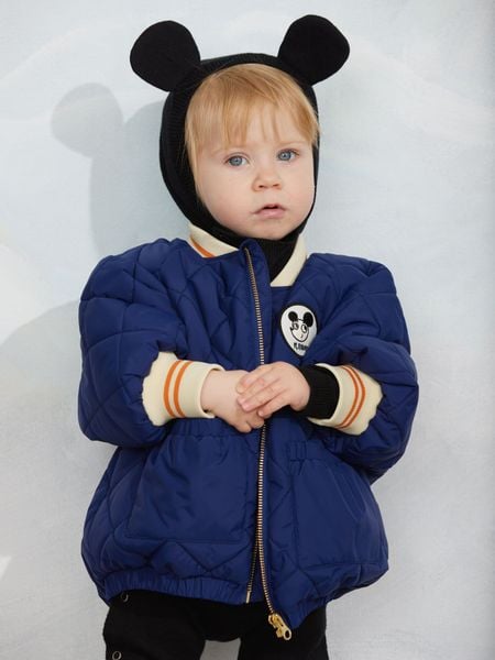 Blue quilted puffer jacket featuring a Ritzratz patch, front zipper, and striped ribbed cuffs.