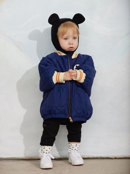 Blue quilted puffer jacket featuring a Ritzratz patch, zipper closure, and striped ribbed cuffs.