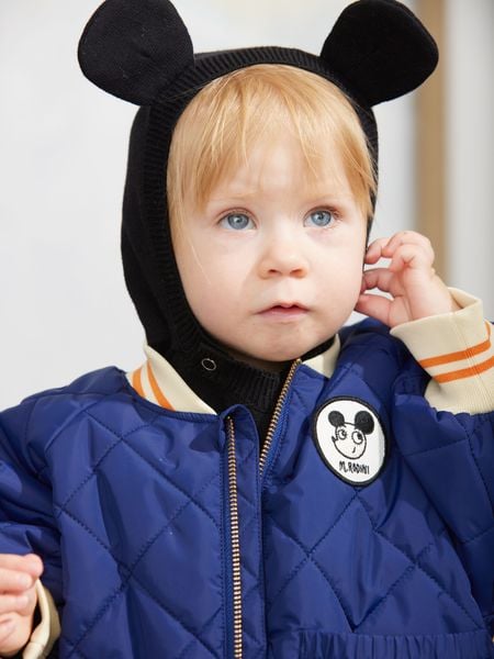 Close-up of a blue quilted puffer jacket with a circular Ritzratz patch and striped ribbed cuffs.