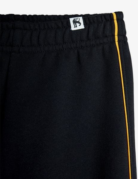 Close-up front view of black sweatpants featuring yellow piping and an elastic waistband.