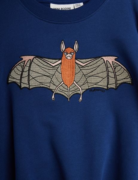 Close-up of a blue sweatshirt featuring an embroidered orange bat with spread wings.