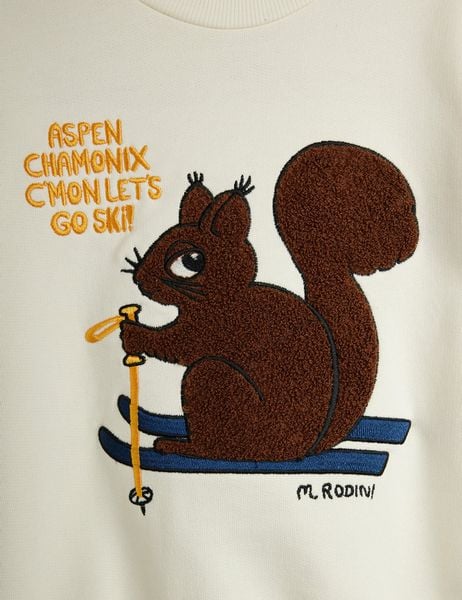 Close-up of a brown chenille skiing squirrel patch on an off-white sweatshirt with text.
